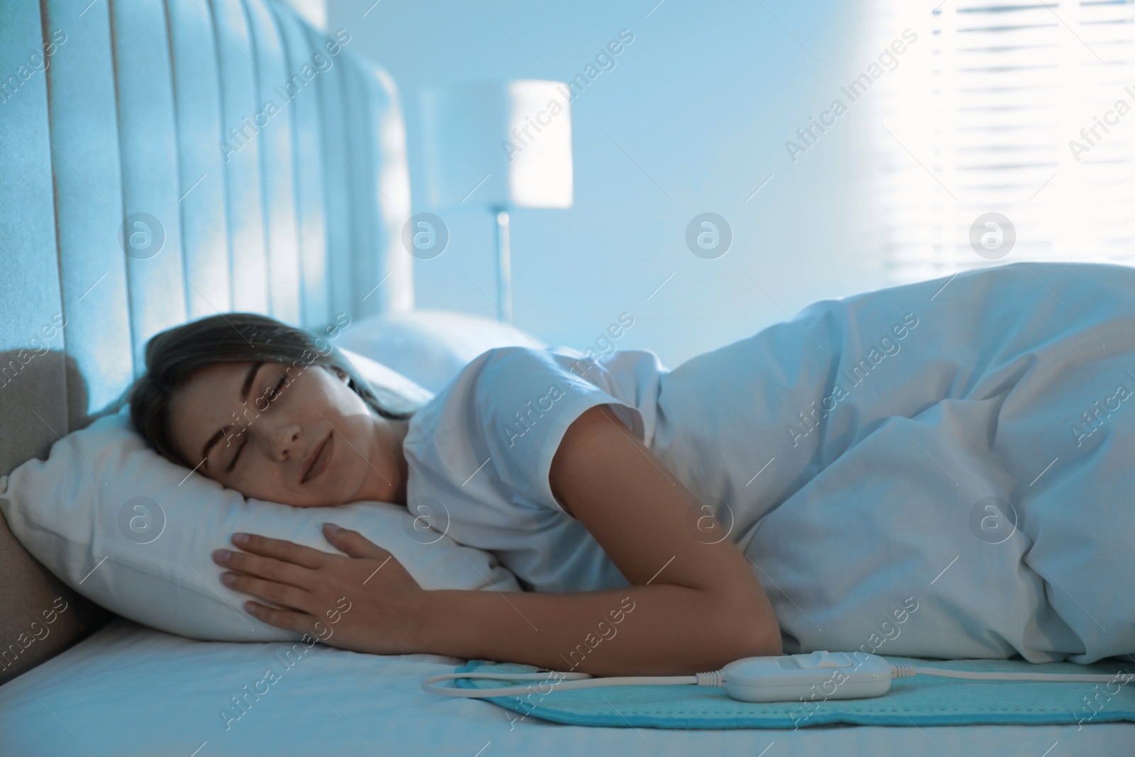 Photo of Young woman sleeping on electric heating pad in bed at night