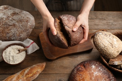 Photo of Woman breaking freshly baked bread at wooden table, closeup