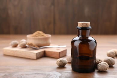 Photo of Bottle of nutmeg oil and nuts on wooden table, space for text