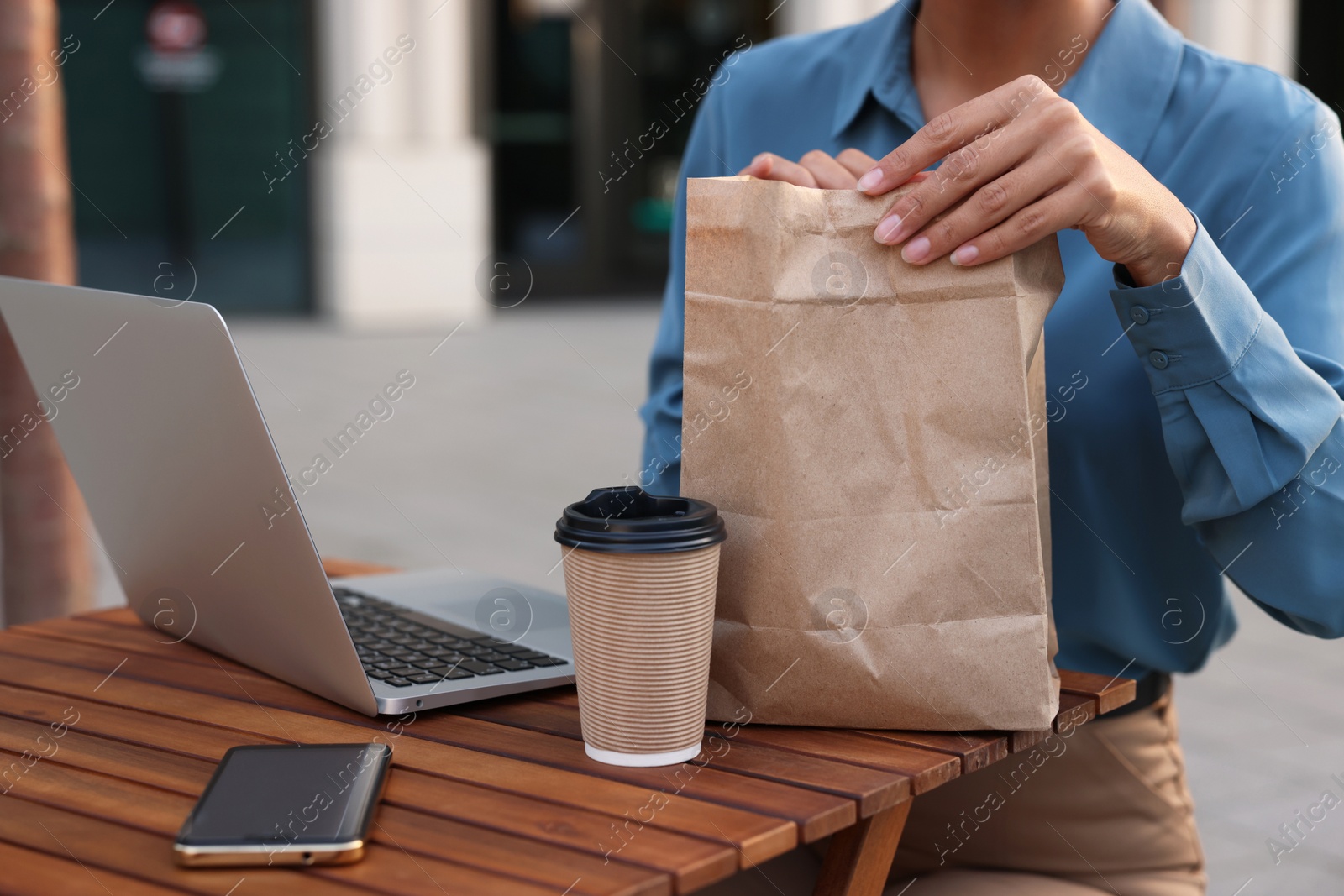 Photo of Businesswoman with paper bag having lunch at wooden table outdoors, closeup