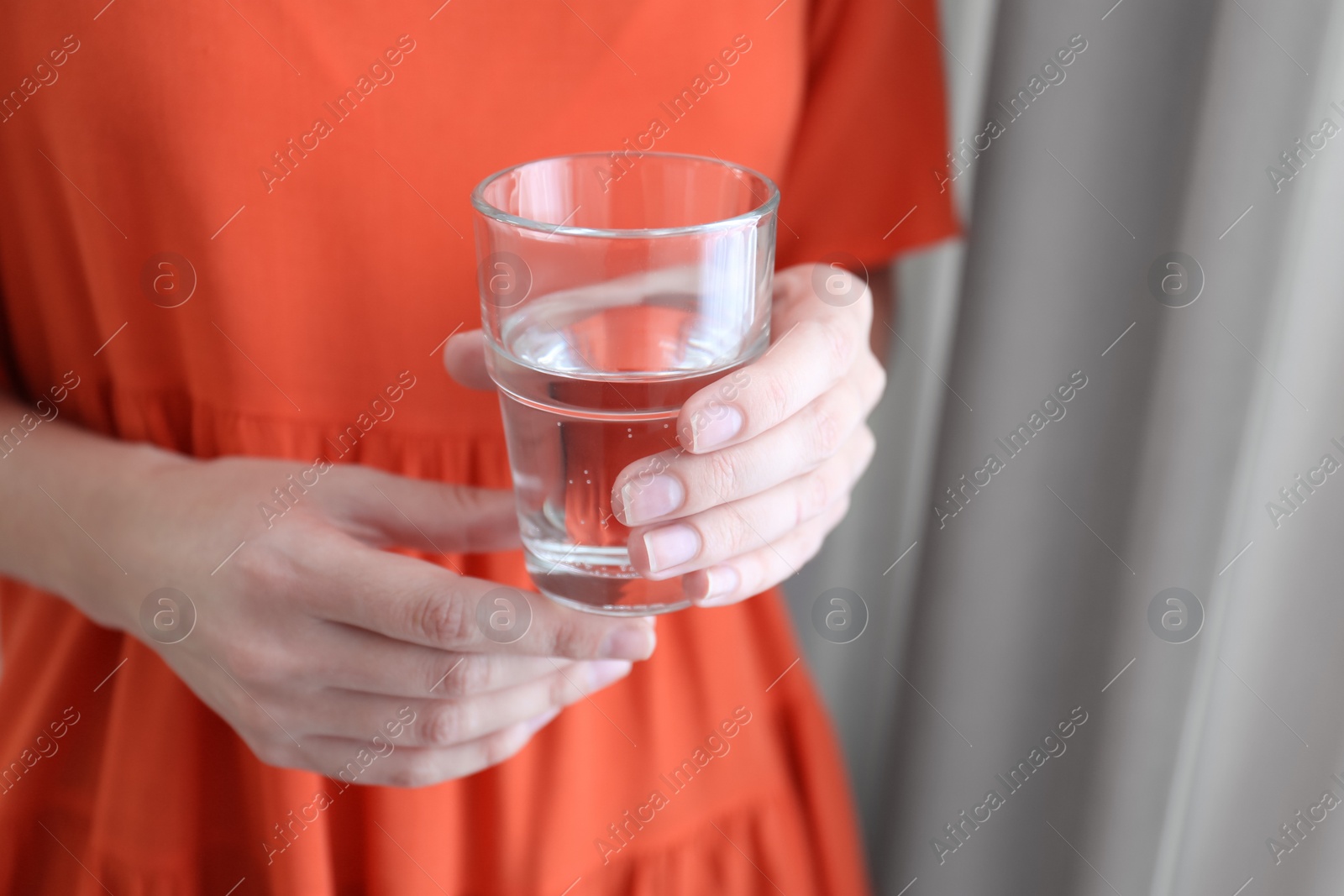 Photo of Woman holding glass of water near window at home, closeup