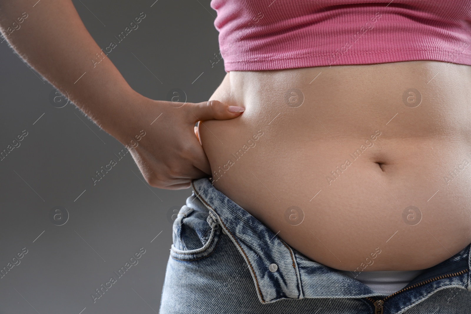 Photo of Woman touching belly fat on grey background, closeup. Overweight problem