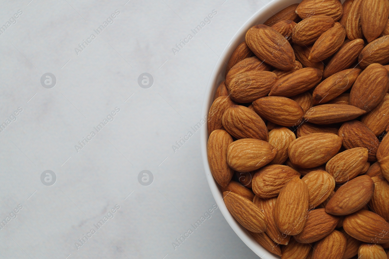 Photo of Bowl of delicious almonds on white marble table, top view. Space for text