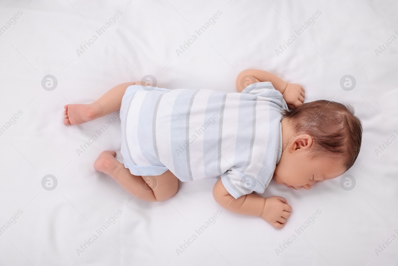 Photo of Cute newborn baby sleeping on white soft bed, top view