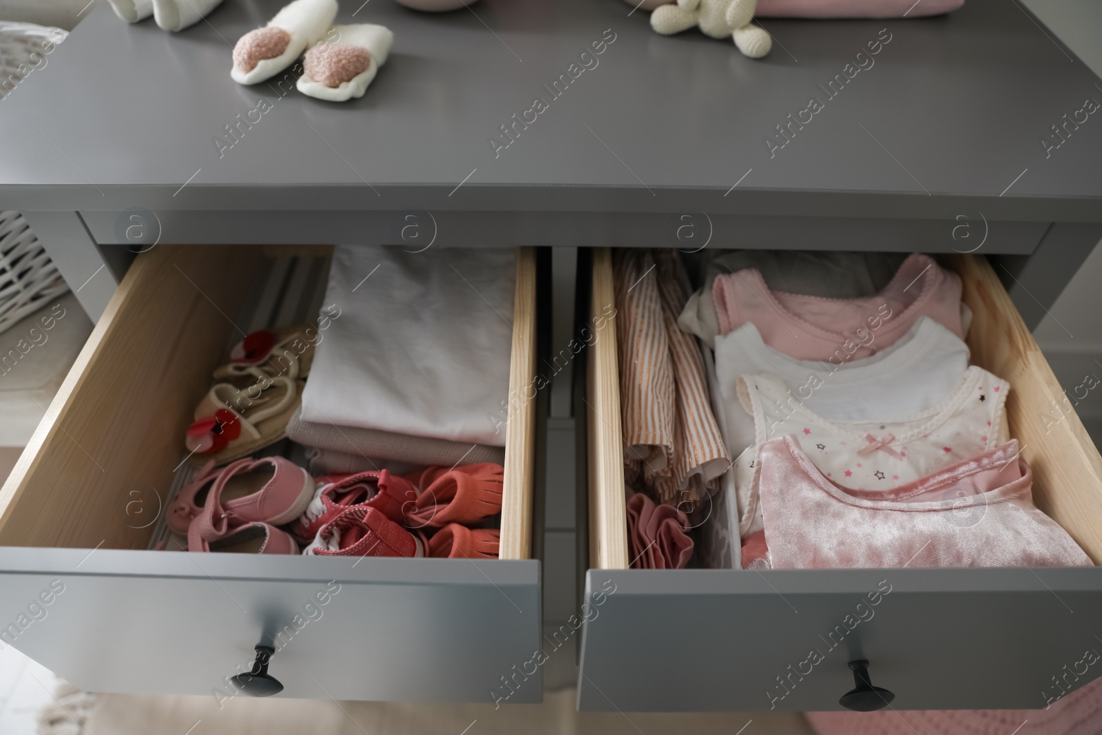 Photo of Open cabinet drawers with baby shoes and clothes in child room