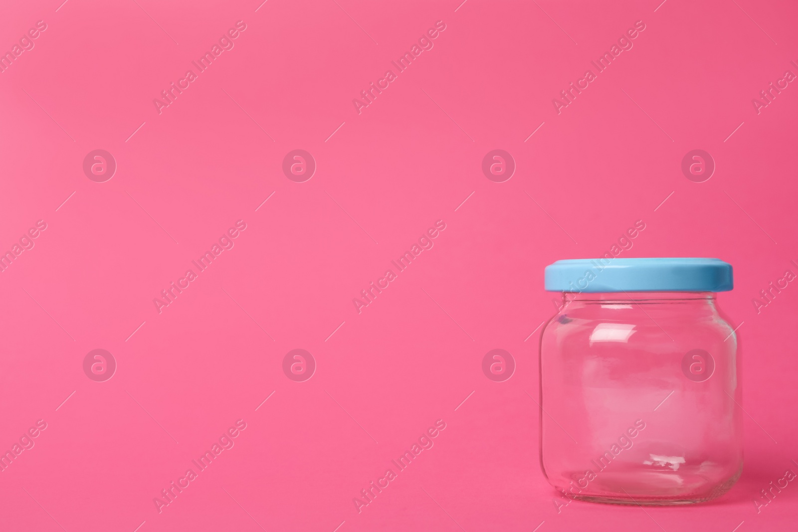 Photo of Closed empty glass jar on pink background, space for text