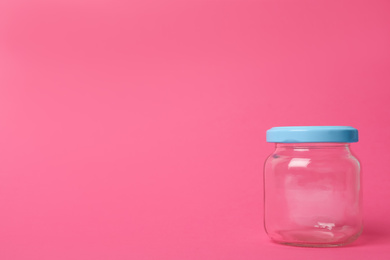 Closed empty glass jar on pink background, space for text