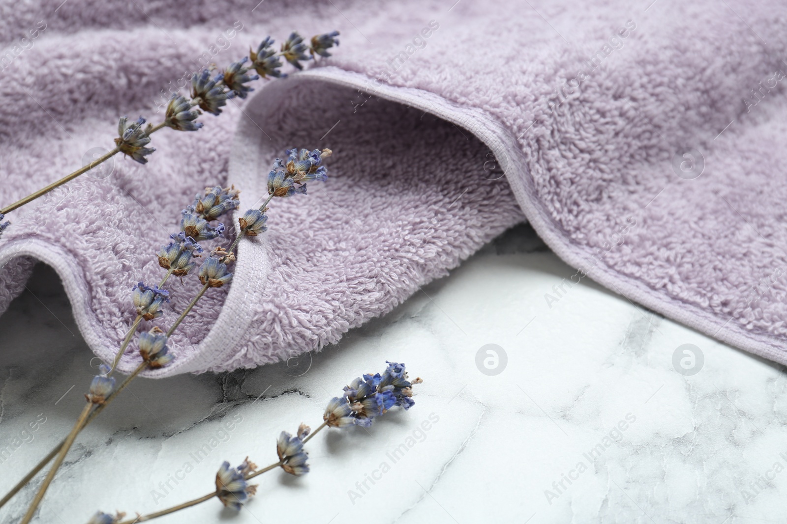 Photo of Violet terry towel and dry flowers on white marble table, closeup