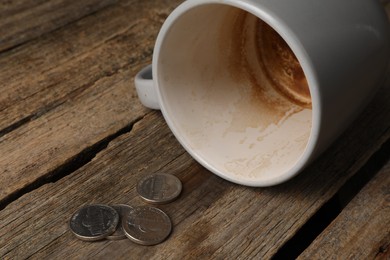Poverty. Overturned dirty cup and coins on wooden table, closeup. Space for text