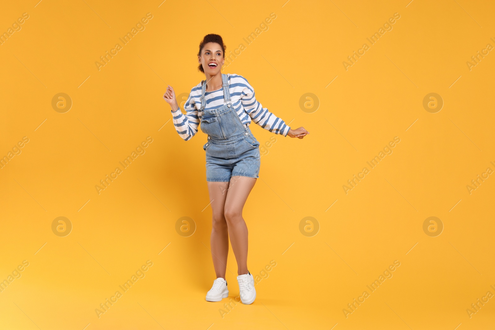 Photo of Happy young woman dancing on orange background