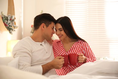 Happy couple with cups in bed. Christmas celebration