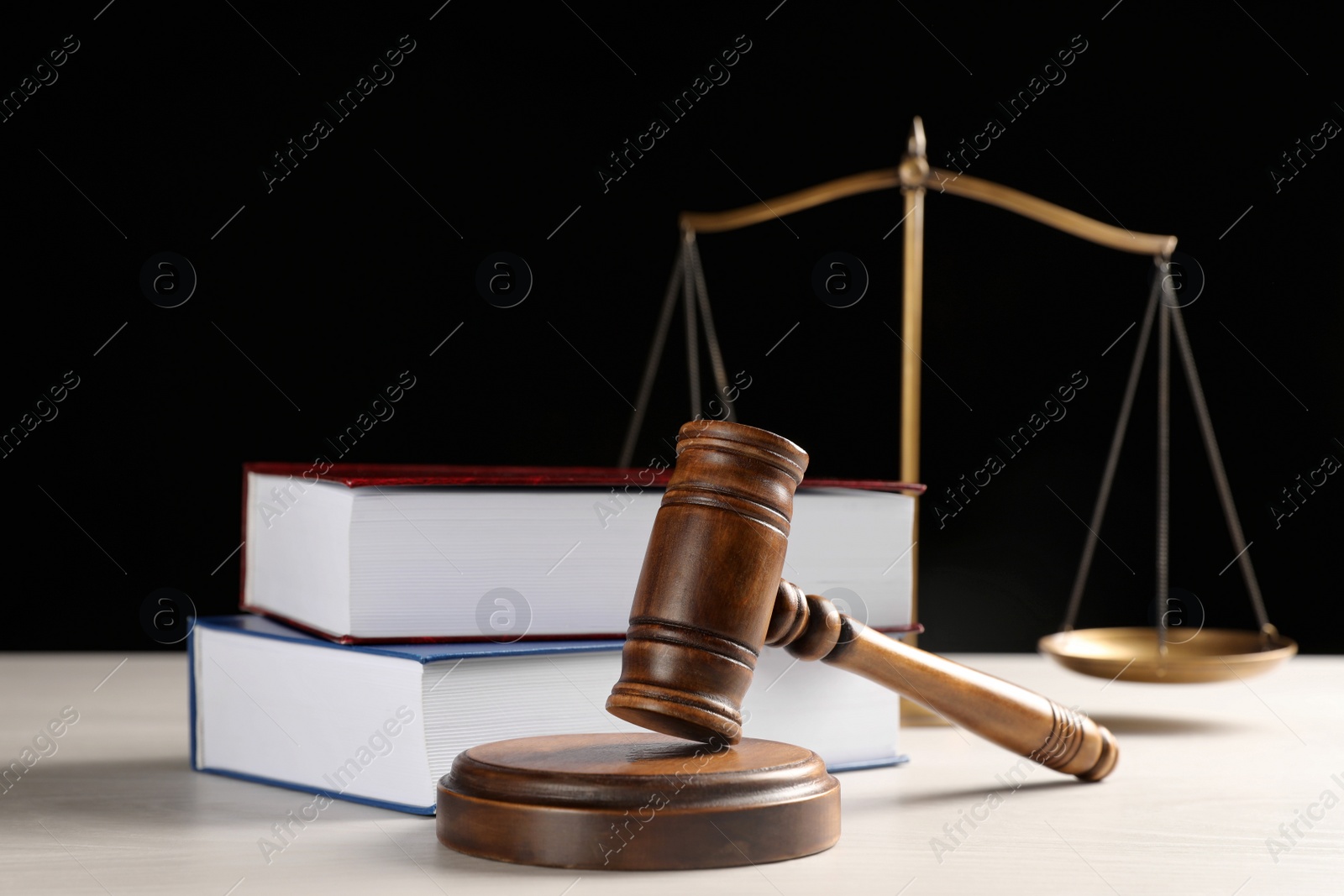 Photo of Judge's gavel, books and scales on white wooden table against black background. Criminal law concept