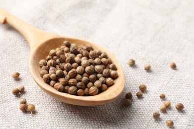 Photo of Spoon with dried coriander seeds on light cloth, closeup