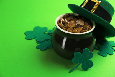 Photo of Pot of gold coins, hat and clover leaves on green background, space for text. St. Patrick's Day celebration