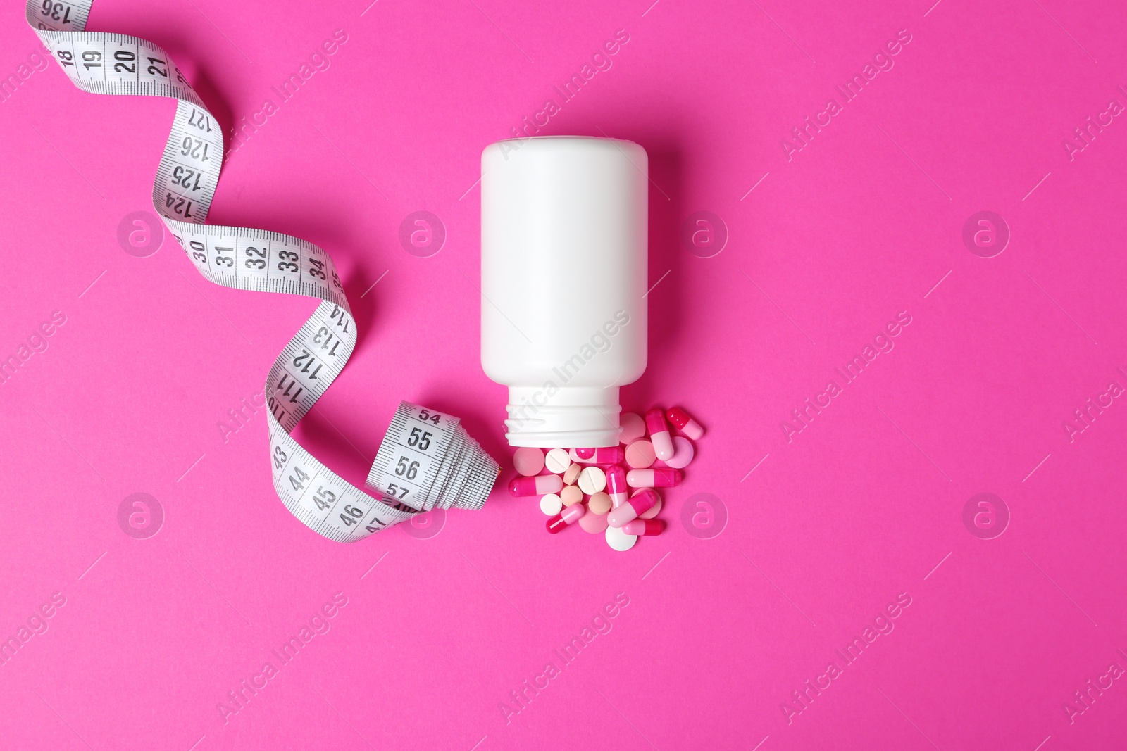 Photo of Weight loss pills, bottle and measuring tape on color background, flat lay