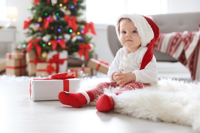 Photo of Cute baby in Santa hat on floor at home. Christmas celebration