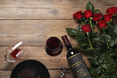 Photo of Bottle and glasses of red wine near beautiful roses on wooden table, flat lay. Space for text