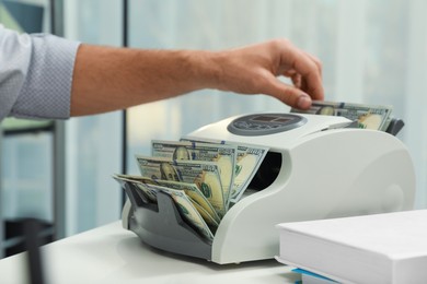 Photo of Man using banknote counter at white table indoors, closeup