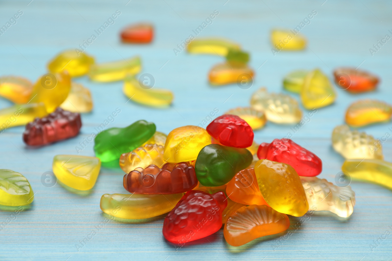 Photo of Delicious gummy fruit shaped candies on light blue wooden table, closeup