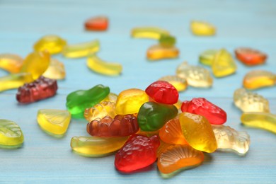 Photo of Delicious gummy fruit shaped candies on light blue wooden table, closeup