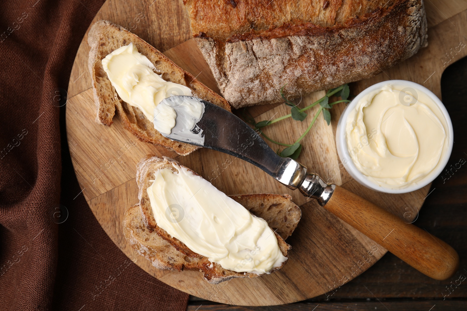Photo of Tasty bread with butter and knife on wooden table, top view