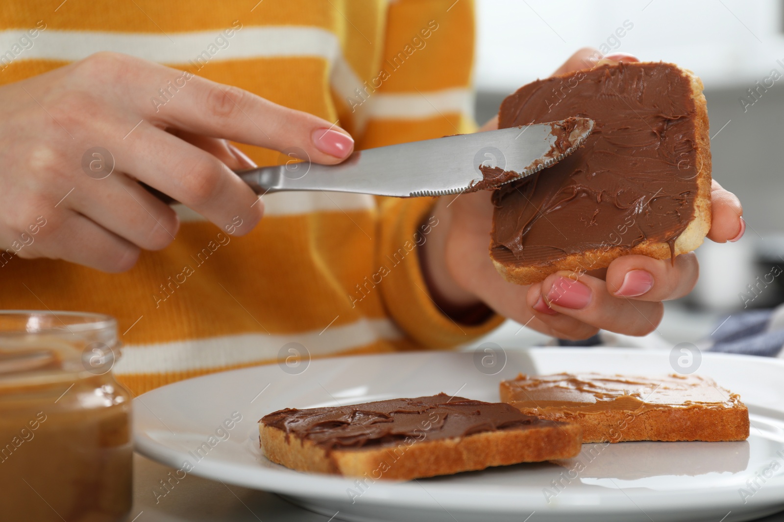 Photo of Woman spreading tasty nut butter onto toast at table, closeup