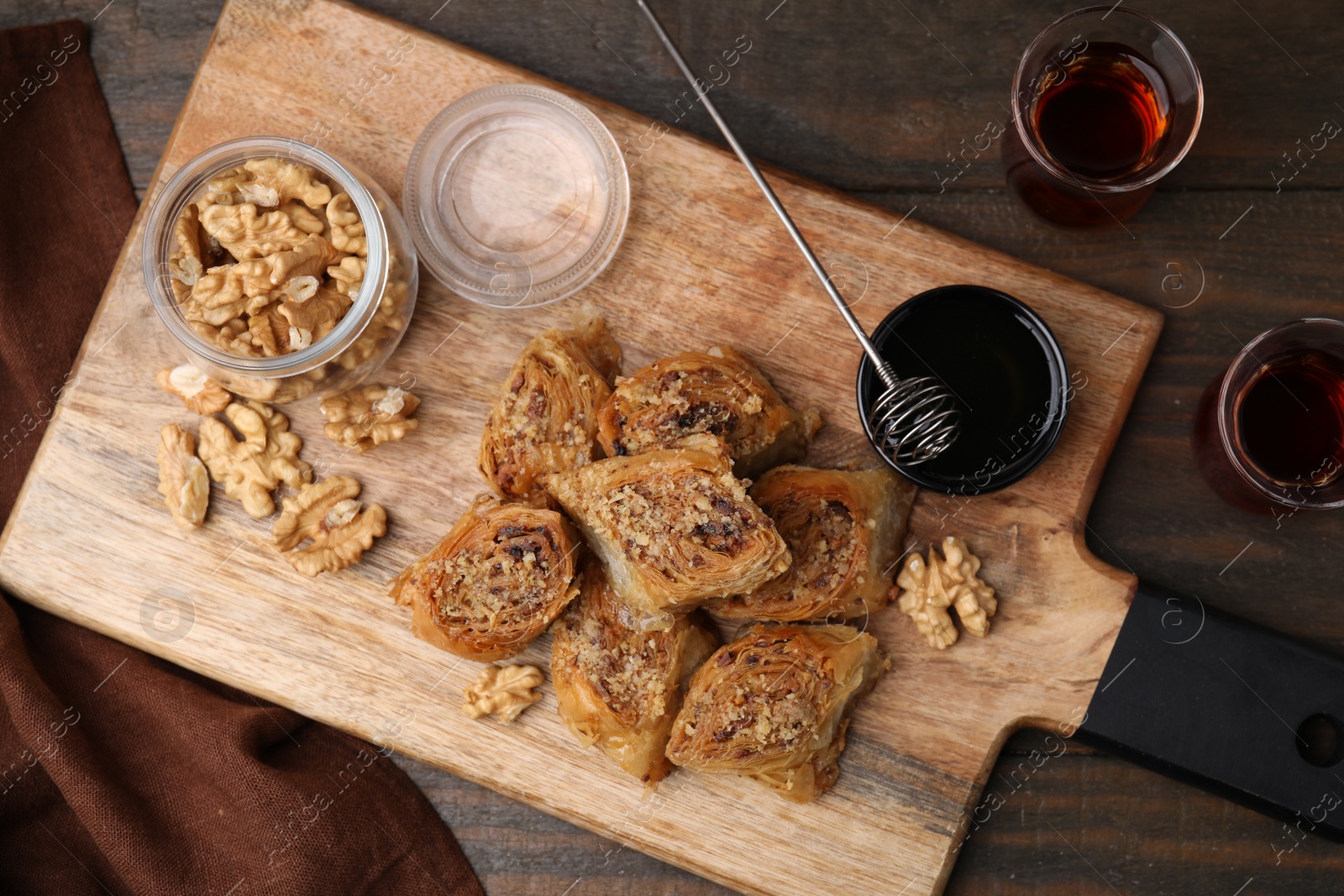 Photo of Eastern sweets. Pieces of tasty baklava, walnuts and tea on wooden table, flat lay