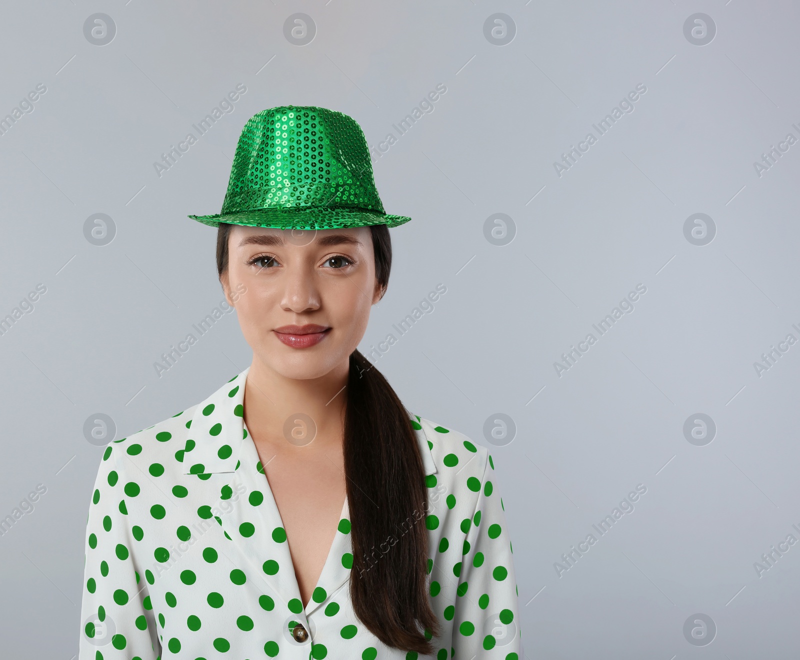 Image of St. Patrick's day party. Pretty woman in green leprechaun hat on grey background. Space for text