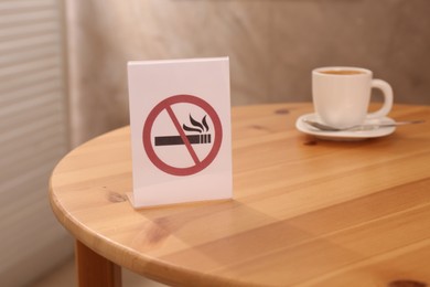 Photo of No Smoking sign and cup of drink on wooden table indoors, selective focus