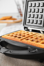 Photo of Modern iron with tasty Belgian waffles on wooden table, closeup