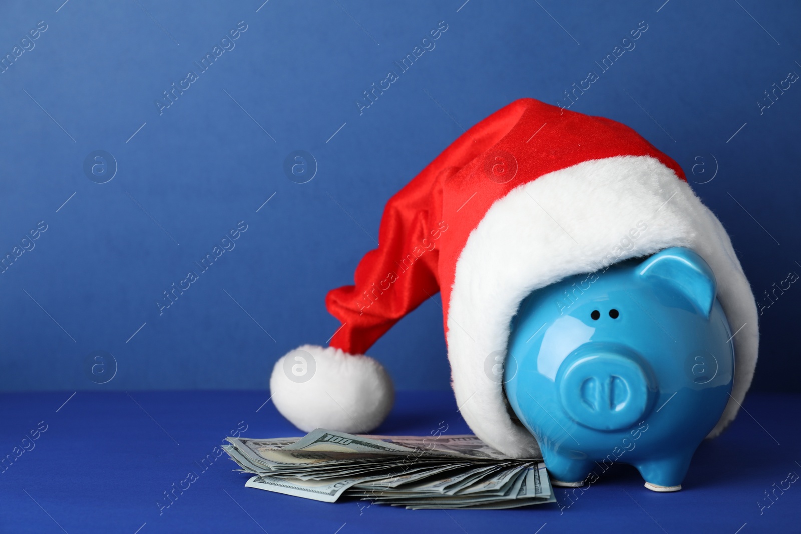 Photo of Piggy bank with Santa hat and dollar banknotes on color background. Space for text