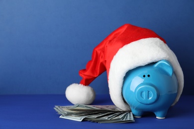 Piggy bank with Santa hat and dollar banknotes on color background. Space for text