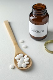 Photo of Calcium supplement pills, spoon and bottle on white table