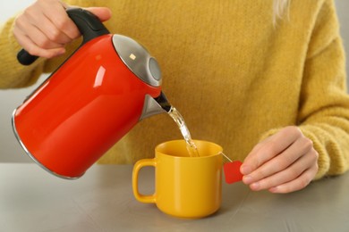 Photo of Woman pouring hot water into cup with tea bag at grey table, closeup