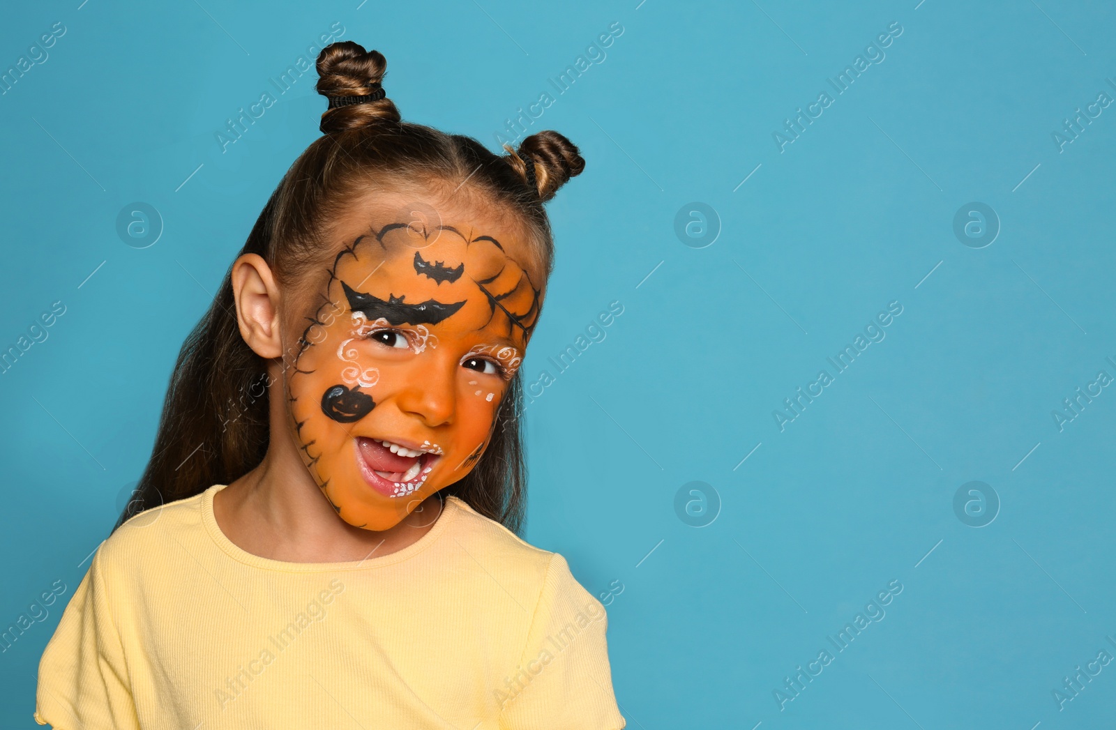 Photo of Cute little girl with face painting on blue background. Space for text