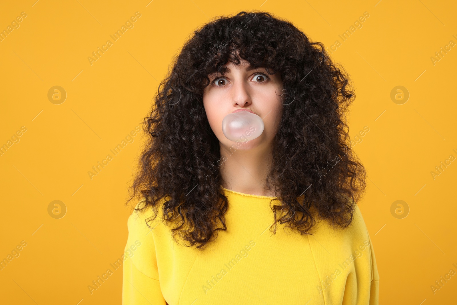 Photo of Beautiful young woman blowing bubble gum on orange background