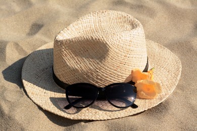 Photo of Hat with beautiful sunglasses and flowers on sand, closeup