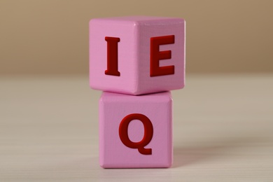 Photo of Pink cubes with letters E, I and Q on white wooden table