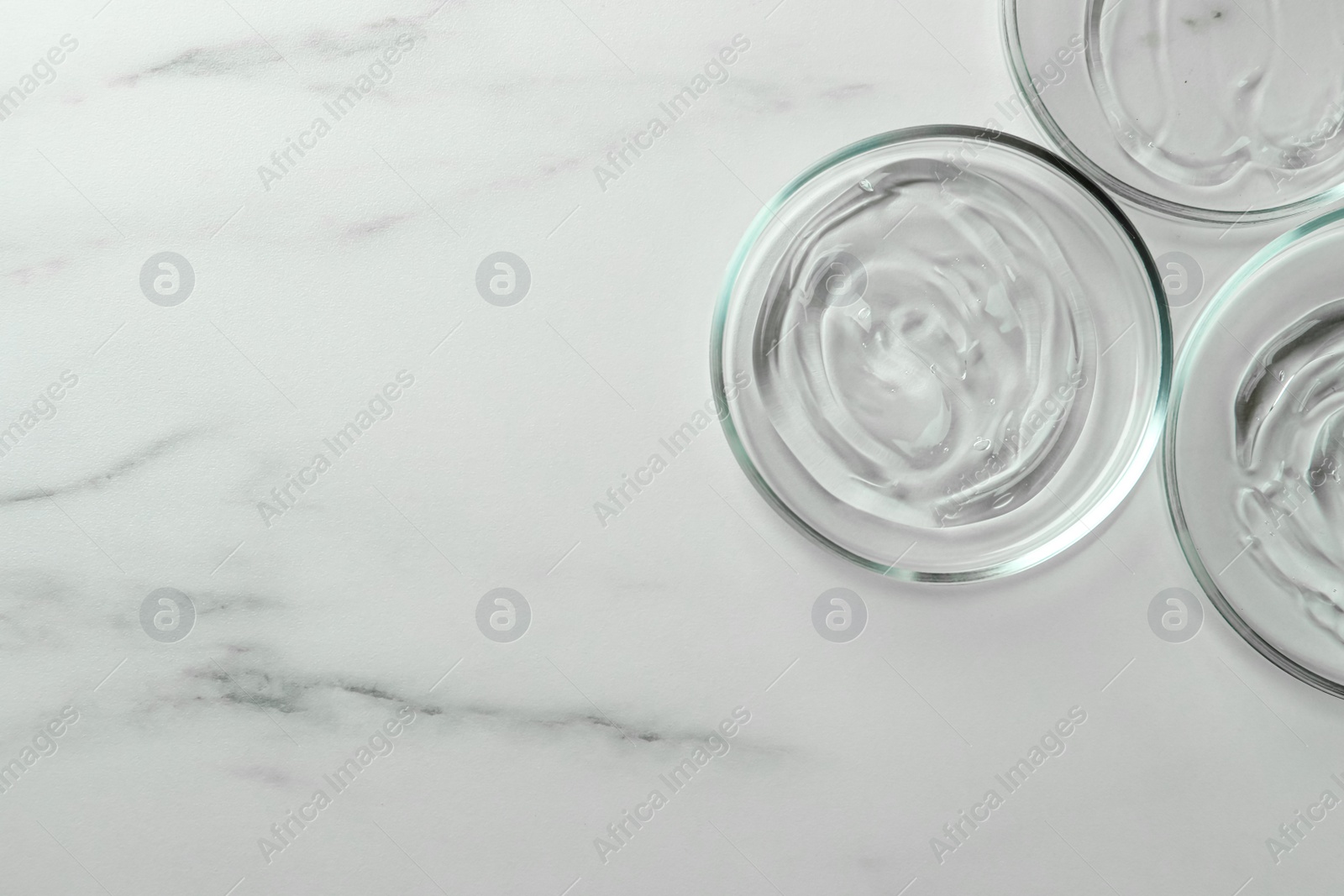 Photo of Petri dishes with liquids on white marble table, flat lay. Space for text