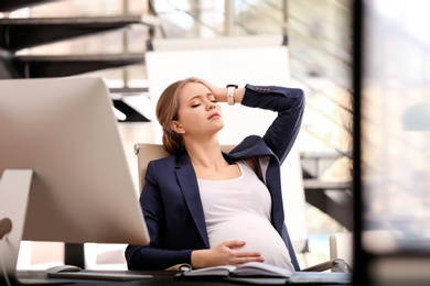 Photo of Young pregnant woman suffering from pain while working in office