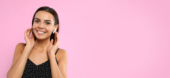 Image of Young woman listening to music with wireless earphones on pink background, space for text. Banner design