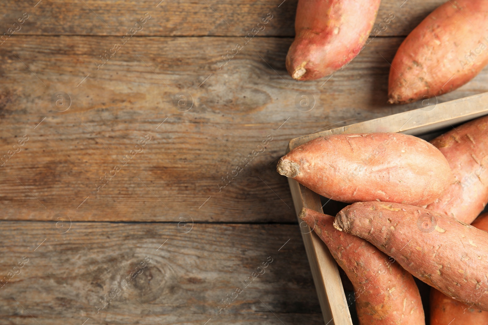 Photo of Crate with sweet potatoes and space for text on wooden background, top view