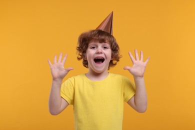 Photo of Emotional little boy in party hat on orange background