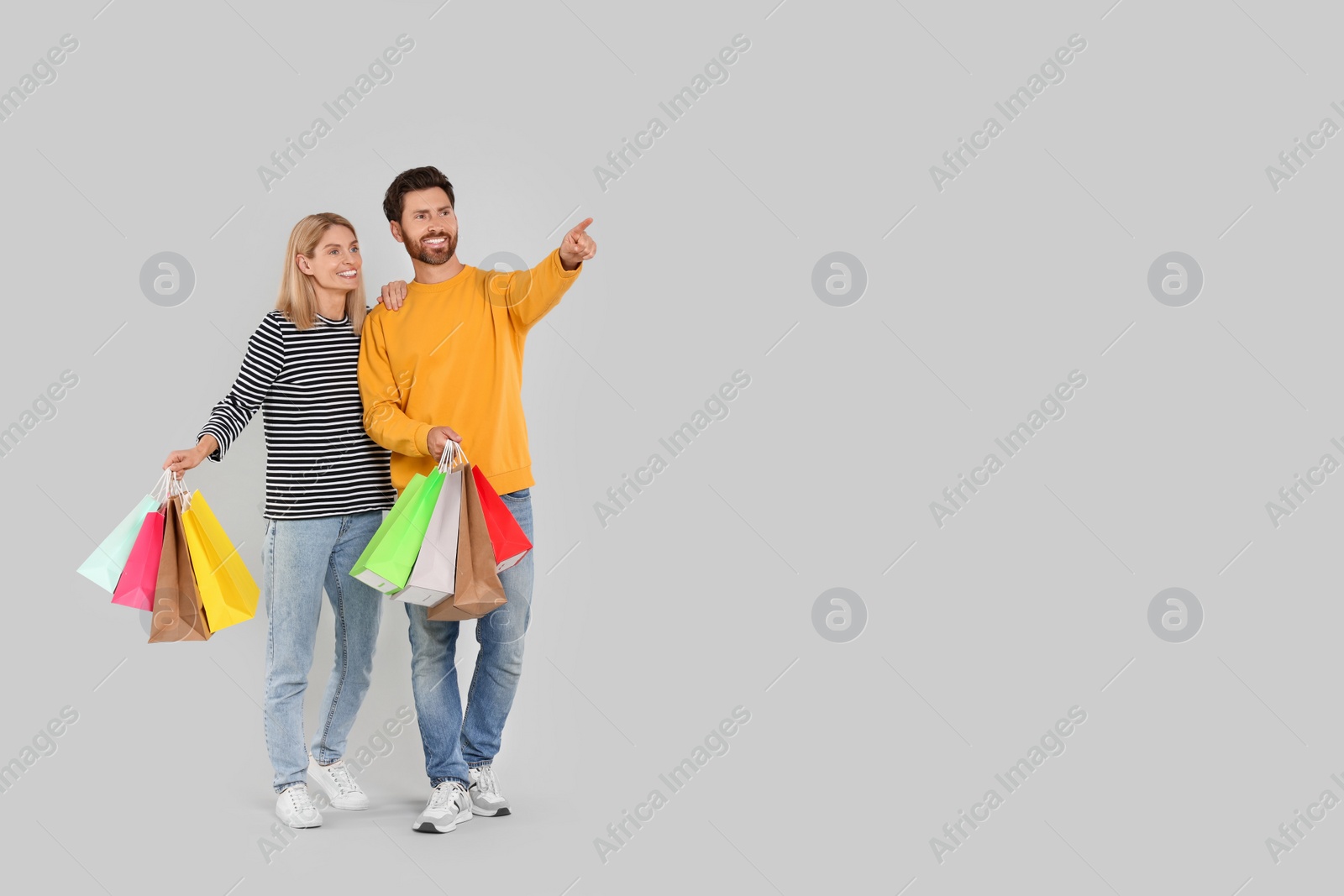Photo of Family shopping. Happy couple with many colorful bags on light grey background. Space for text