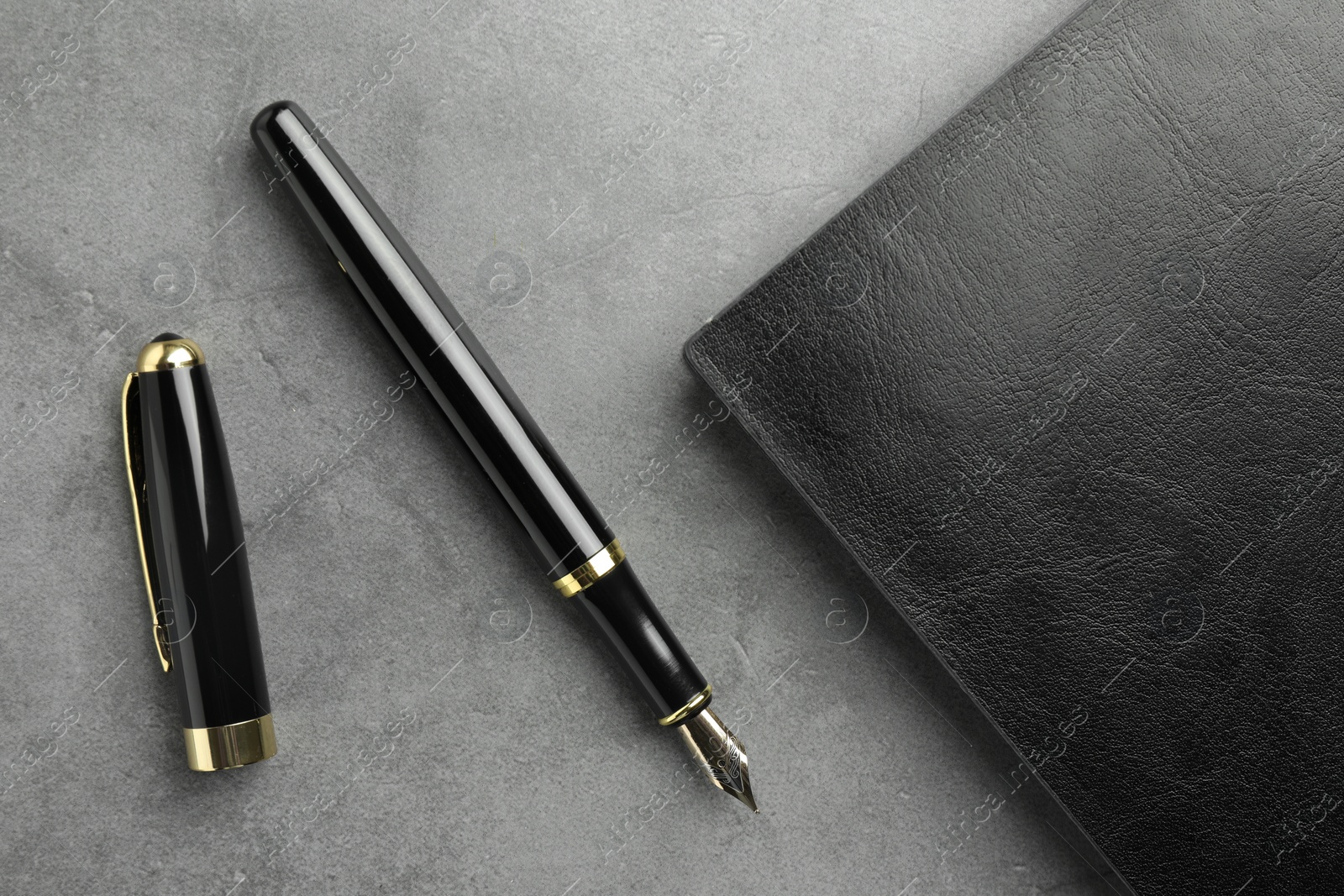 Photo of Stylish fountain pen, cap and leather notebook on light grey textured table, flat lay