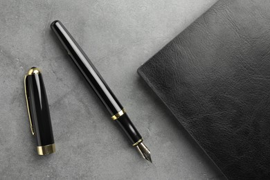 Photo of Stylish fountain pen, cap and leather notebook on light grey textured table, flat lay