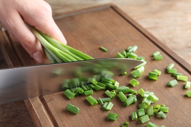 Photo of Woman cutting fresh green onion on wooden board at table, closeup