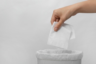 Photo of Woman putting paper tissue into trash bin on light background, closeup