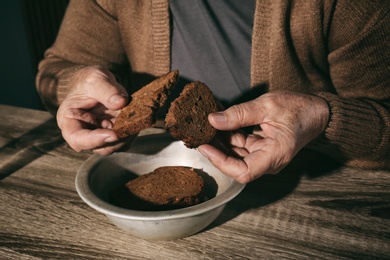 Poor senior woman with bread at table, closeup