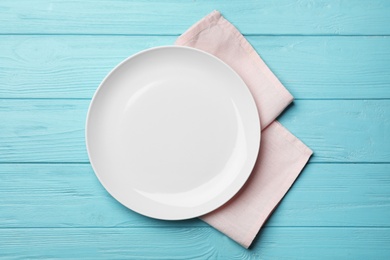 Stylish ceramic plate and napkin on color wooden background, flat lay